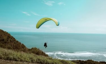 person in black shirt on yellow parachute over blue sea under blue sky during daytime