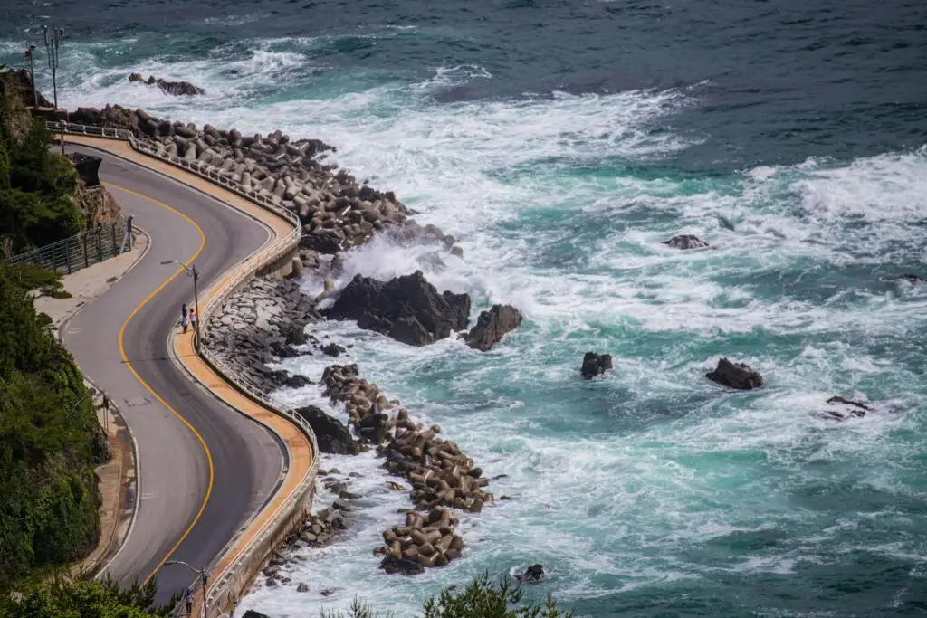 a road next to the ocean with waves crashing on it