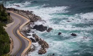 a road next to the ocean with waves crashing on it